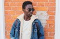 Portrait stylish young african man model wearing denim jacket posing on a city street over brick wall background Royalty Free Stock Photo