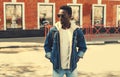 Portrait of stylish young african man posing wearing denim jacket, backpack on city street background Royalty Free Stock Photo