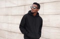 Portrait stylish young african man walking and looking away wearing a black hoodie, sunglasses on a city street over gray wall Royalty Free Stock Photo