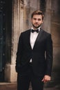 Portrait of a stylish young groom in an old European town. man in a stylish suit with bow tie near old building. wedding day