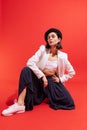 Portrait of stylish young woman in beret and jacket posing isolated over red studio background. Parisian outfit