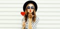 Portrait of stylish young woman blowing her red lips sending air kiss with red heart shaped lollipop wearing black round hat, Royalty Free Stock Photo