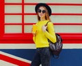 Portrait of stylish young woman with cup of juice wearing yellow sweater, black round hat over background Royalty Free Stock Photo