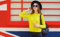 Portrait of stylish young woman with cup of juice wearing yellow sweater, black round hat over background Royalty Free Stock Photo