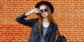 Portrait of stylish young woman model blowing lips wearing a black round hat, jacket in the city over brick background Royalty Free Stock Photo