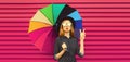 Portrait of stylish young woman model posing with colorful umbrella wearing black round hat blowing her lips sends kiss on pink Royalty Free Stock Photo