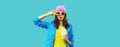 Portrait of stylish young woman model posing with cup of coffee or juice wearing colorful pink hat, jacket on blue background Royalty Free Stock Photo