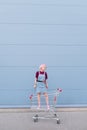 Portrait of a stylish young woman with pink hair standing in a cart on the background of a blue wall. Street fashion Royalty Free Stock Photo