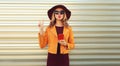 Portrait of stylish young woman posing blowing her lips sends sweet air kiss holds phone wearing sunglasses, round hat and jacket Royalty Free Stock Photo