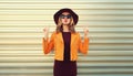 Portrait of stylish young woman posing blowing her lips sends sweet air kiss wearing sunglasses, round hat and jacket on gray Royalty Free Stock Photo
