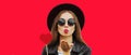 Portrait of stylish young woman with red heart shaped lollipop blowing her lips sending sweet air kiss wearing a black round hat Royalty Free Stock Photo