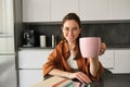 Portrait of stylish young woman, student shares her cup of coffee, gives you mug, smiling and looking happy