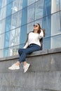 Portrait of stylish young woman in sunglasses on city street. Young girl on background of glass facade of the building