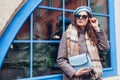 Portrait of stylish young woman wearing beret coat holding blue purse outdoors. Spring fashion female retro accessories