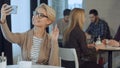 Portrait of stylish young woman wearing glasses sitting at cafe and taking selfie with her smart phone Royalty Free Stock Photo