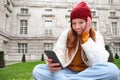Portrait of stylish young woman, 25 years, sits on bench in park and uses mobile phone, reads online news, messages or Royalty Free Stock Photo