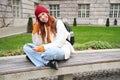 Portrait of stylish young woman, 25 years, sits on bench in park and uses mobile phone, reads online news, messages or Royalty Free Stock Photo