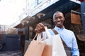 Smiling young man standing outside holding up shopping bags Royalty Free Stock Photo