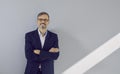 Portrait of succesful mature businessman in suit and glasses standing near wall in office.