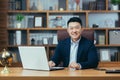 successful Asian businessman, man working in the office sitting at the table, looking at the camera and smiling, Royalty Free Stock Photo