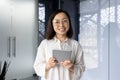 Portrait of successful asian female programmer inside office, young woman smiling and looking at camera, using tablet Royalty Free Stock Photo