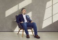 Portrait of successful confident mature businessman sitting on chair by grey office wall Royalty Free Stock Photo