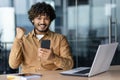 Portrait of successful hispanic young businessman, man smiling and looking at camera at workplace holding phone Royalty Free Stock Photo