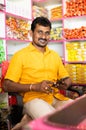 Portrait of successful Indian kirana or groceries businessman sitting on counter with smile by looking at camera -