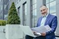 Portrait of successful investor behind paperwork, man outside office building