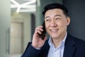 Portrait of successful mature asian businessman inside office at workplace, senior boss talking on phone, smiling, man Royalty Free Stock Photo