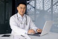 Portrait of a successful senior doctor working inside a clinic using a laptop, adult mature Asian man in glasses and a Royalty Free Stock Photo