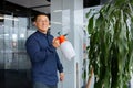 Portrait of successful smiling asian man inside office, boss watering flowers spraying flower pot with sprayer Royalty Free Stock Photo