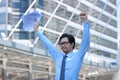 Portrait of successful young Asian business man raising hands with charts or paperwork at urban city background. Royalty Free Stock Photo