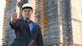 Portrait of a successful young handsome engineer, architect, builder, businessman, wearing a white helmet, in a suit, holding a pr