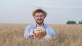 Portrait of sucessful agronomist, young man gives you freshly baked bread and smiles at camera in wheat crop field