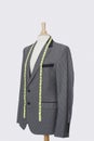 Suit on tailor`s dummy with measuring tape over gray background