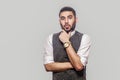 Portrait of suprised handsome bearded brunette man in white shirt and waistcoat standing, holding his chin and looking at camera Royalty Free Stock Photo