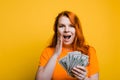 Portrait of a suprised young woman holding banknotes, yellow background. Royalty Free Stock Photo