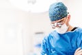 Portrait of surgeon, cosmetic plastician looking down with surgical lamps in background. Doctor with loupes