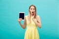 Portrait of a surprised amazed young woman looking at digital tablet isolated on a blue studio background.