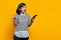 Portrait of surprised asian woman holding mobile phone with confused and unhappy expression on yellow background Royalty Free Stock Photo