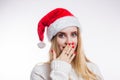 Portrait of surprised attractive young woman in red Santa hat and beige sweater on white background. A girl with a bright manicure Royalty Free Stock Photo