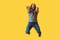 Portrait of surprised bearded young man with long curly hair in grey tshirt jumping, pointing and looking at camera with amazed Royalty Free Stock Photo