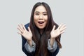 Portrait of surprised beautiful brunette asian young woman in blue jacket with makeup standing with raised arms and looking at Royalty Free Stock Photo