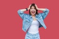 Portrait of surprised beautiful brunette young woman with makeup in denim casual style standing, holding her head, looking at Royalty Free Stock Photo