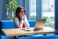 Portrait of surprised beautiful stylish brunette young woman in glasses sitting, reading amazing news on her laptop screen and Royalty Free Stock Photo