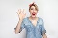 Portrait of surprised beautiful young woman in casual blue denim shirt with makeup and red headband standing, happy and waving