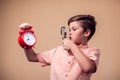 A portrait of surprised boy looking through magnifier at alarm clock. Children and time management concept Royalty Free Stock Photo