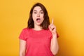 Portrait of surprised brunette woman pointing up with her fore finger while looking directly at camera isolated over yellow Royalty Free Stock Photo