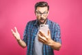 Portrait of a surprised casual man looking at mobile phone isolated over pink background